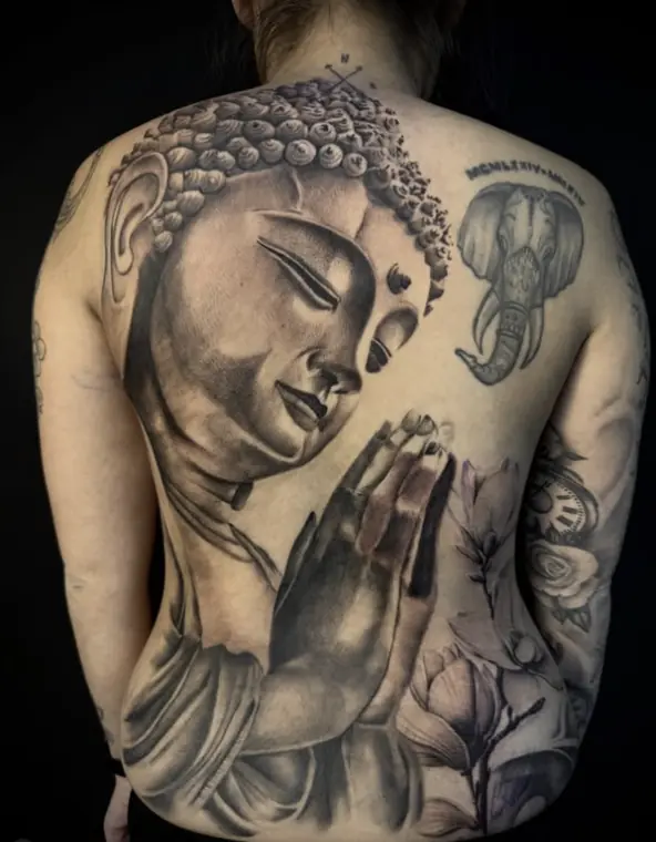 A full back piece of a Buddha with hands in prayer, rendered in soft black and grey with magnolia blossoms.