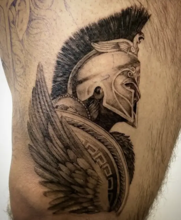 A helmeted Spartan warrior in profile with a winged shield, on the thigh.